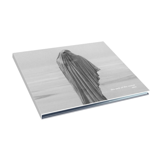 A minimalist album cover for The End Of The Ocean, showing a black and white figure draped in fabric on a beach. "the end of the ocean" and "aire" appear in lowercase in the bottom right, evoking quiet redemption.